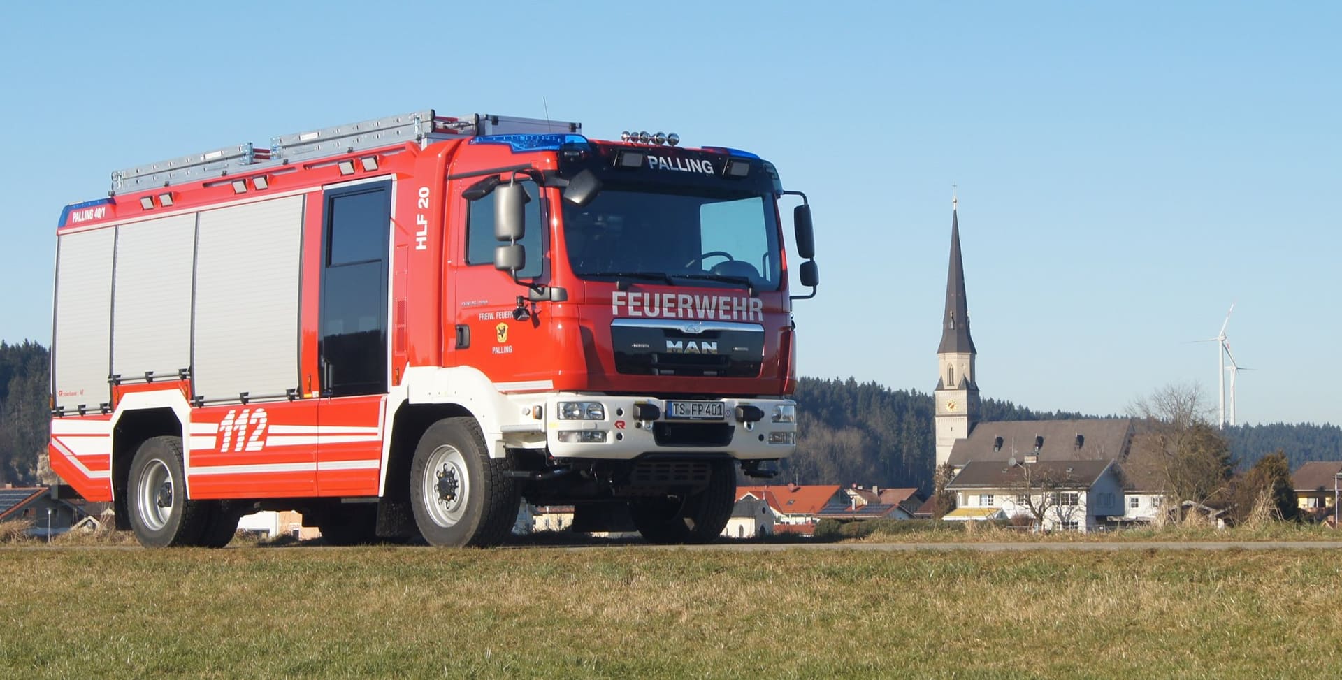 Das Hilfeleistungslöschgruppenfahrzeug HLF 20 der Feuerwehr Palling auf einer Wiese, im Hintergrund ein Kirchturm